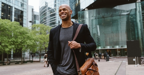 happy african american man walking to the office building, while smiling and carrying a messenger bag.