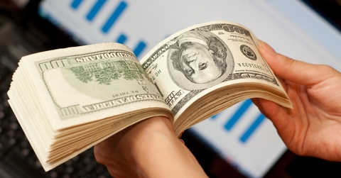 man skimming through cash notes in hand with laptop in background