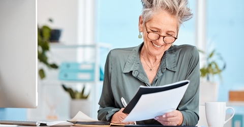 happy senior business woman sitting in office making notes while holding file