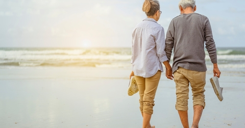 senior couple walking on beach while holding each others hand