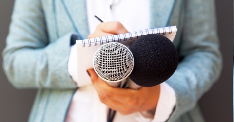 female journalist holding mics while making notes for interview