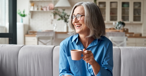 grey-haired woman drinking coffee relaxing on sofa