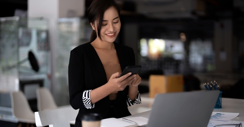Business asian woman using mobile phone with a laptop on the table,while working in her office