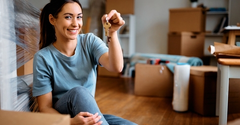 a young woman, brimming with joy, holding a key while moving into her new home with cardboard boxes filled with packed luggage.