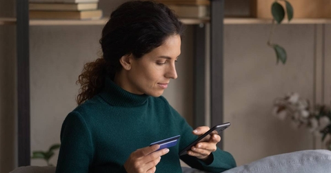 Focused young woman holding a smartphone in one hand and a card with another hand.