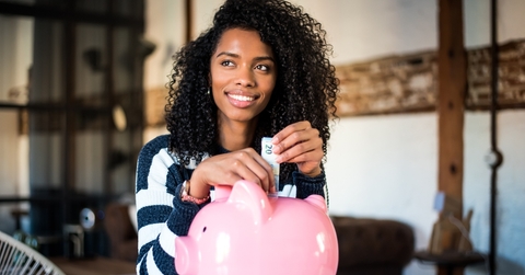 Smiling woman putting money in a piggy bank