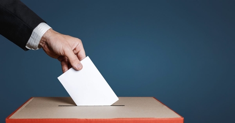 A voter puts a ballot into a ballot box. 