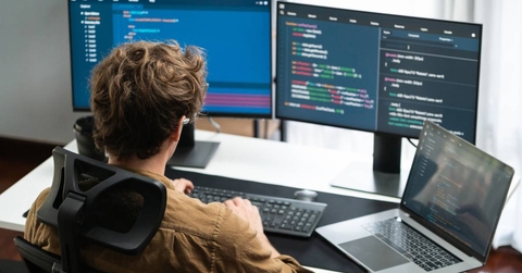  man working from home on pc monitors at modern home office doing coding