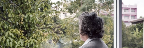 elderly woman looking out window longingly