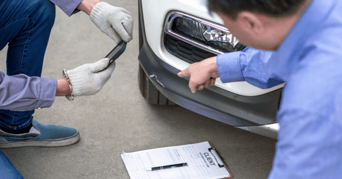 Two individuals inspect damage on a vehicle