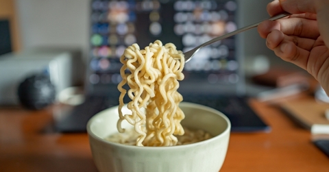 man eating ramen with laptop at work