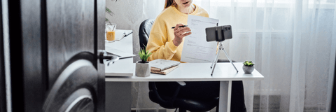 A young woman holds up a piece of paper as she speaks in front of her iPhone on a tripod. 