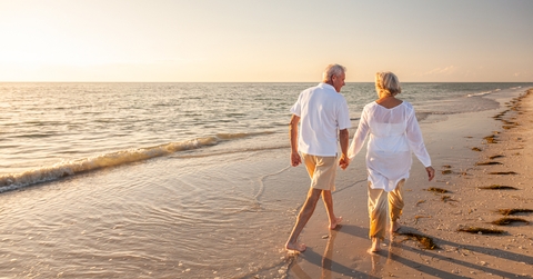retired couple walking holding hands on beach