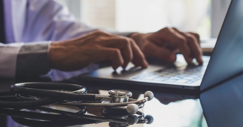 male doctor typing on laptop with medical stethoscope on the desk