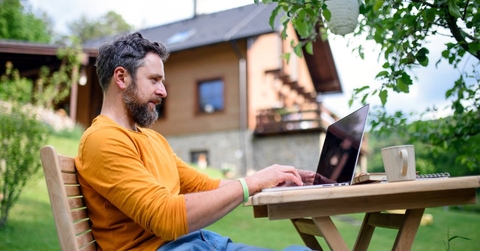 Side view of man with laptop working outdoors in garden, home office concept
