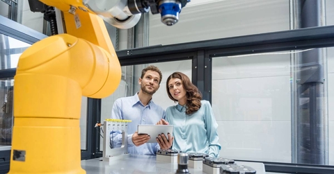 Colleagues in high tech company controlling industrial robots, using digital tablet