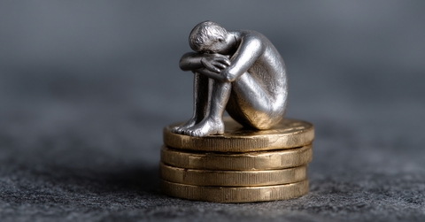 sad person silver figure sits atop of coins