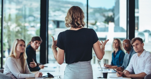 Business woman standing with its back to camera speaking to table of people