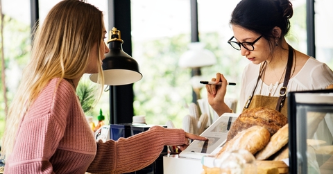 Woman paying on tablet at the bakery with register employee watching