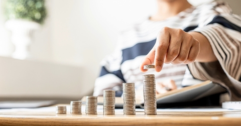 Woman adding coins to the last pile as it slowly shows growth of wealth