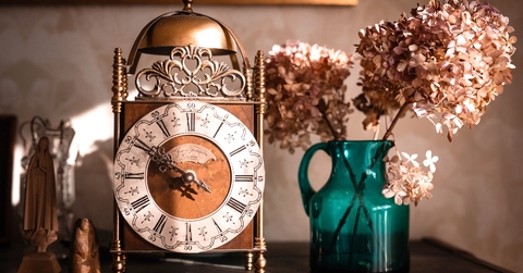 Old clock on the shelf next to flower vase